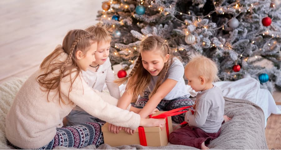 Children opening a gift in the family room beside a Christmas tree.